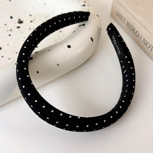 Macro detail of a handmade satin polka dot headband with a woven label on a ceramic tray