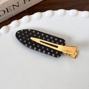 Close-up of polka dot acrylic hair clip with golden metal clip on a ceramic tray