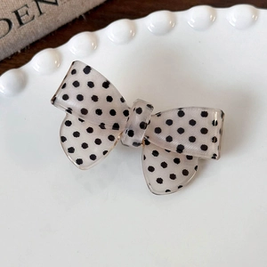 Detail of a creamy polka dot bow hair clip with translucent fabric in a ceramic dish