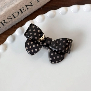 Close-up of a black and white polka dot bow hair clip on a white ceramic plate
