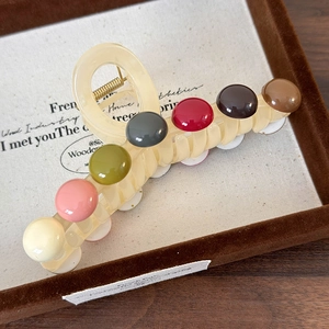 Détail d'une pince à cheveux à perles colorées posée sur un plateau vintage français