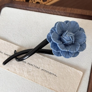 Gros plan d'une pince à cheveux fleur camélia en denim bleu sur un plateau en bois