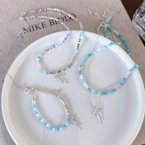 Blue beaded necklace with silver bow pendant on white plate and linen background
