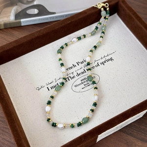 Peacock green stone bead and baroque pearl necklace with golden clasp in a tray