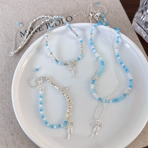 Elegant blue beaded necklace with silver bow pendants and pearl accents on a white plate