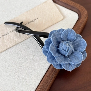 Gros plan détaillé d'une pince à cheveux fleur en denim bleu et résine noire polie