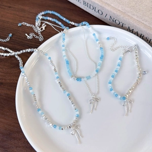 Blue beaded necklace and bracelet set featuring silver bow pendants on a ceramic plate