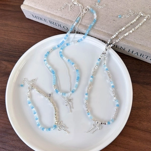 Detail view of light blue beaded necklaces with silver bow charms in a white ceramic dish