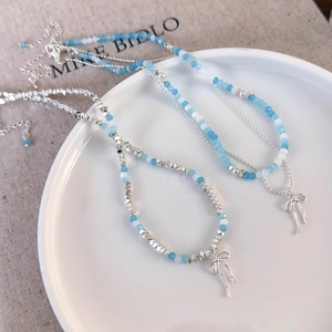 Detailed view of sky blue beads and silver bow pendants on a light aesthetic necklace
