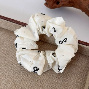 Detail of cream fabric scrunchie with black bow print and silver metal rivets