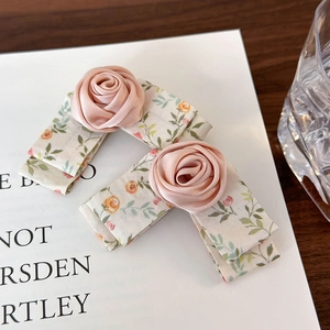 Detailed close-up of pink satin rose hair clips with floral bow on a white vintage paper