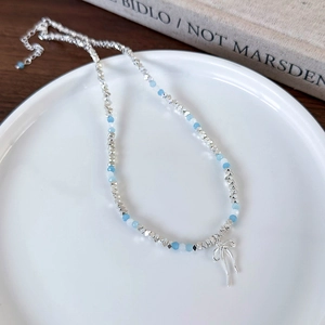 Blue beaded necklace with silver bow pendant on a ceramic plate with book background