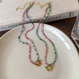 Colliers de perles colorées avec pendentifs papillon en émail sur un plat en céramique