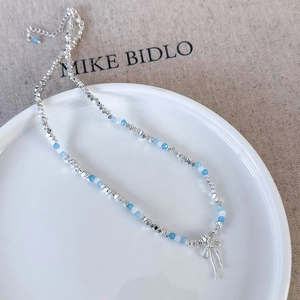 Close-up of blue beaded necklace with silver bow pendant on ceramic tray