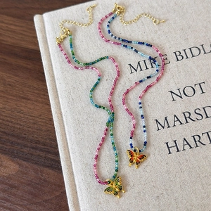 Détail de colliers de perles colorées bohèmes avec pendentif papillon émaillé et fermoir doré