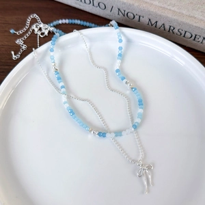 Detail of blue beaded bow necklace with silver beads on a white ceramic plate