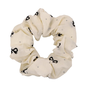 Cream fabric scrunchie with black bow prints and silver rhinestones on white background