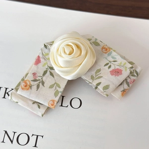 Detail of handmade cream fabric rose hair clip with floral ribbon on magazine background