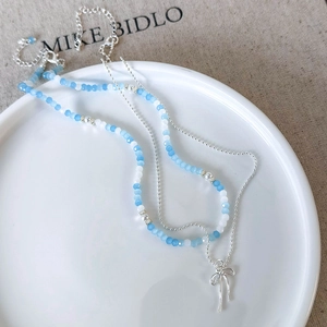 Detailed close-up of double-layer necklace with blue beads and a silver bow pendant