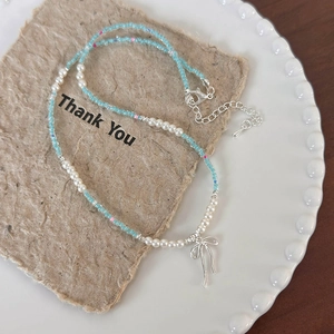 Detail of beaded pearl necklace with silver bow pendant on vintage paper and plate