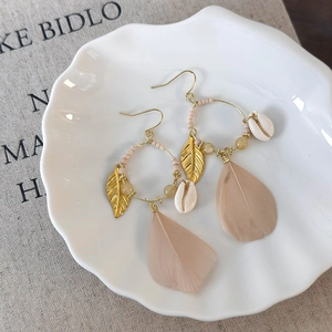 Detail of bohemian gold earrings with natural white shells and beige feathers in a tray
