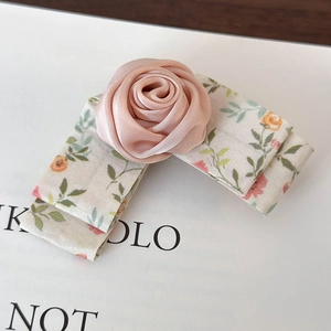 Detail of a handmade pink satin rose hair clip with floral ribbon on display card