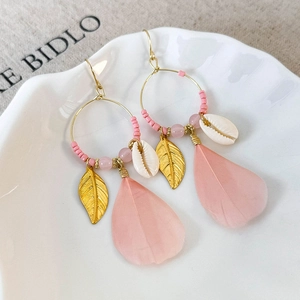 Detail of bohemian pink feather earrings with gold hoops, shells, and delicate beads