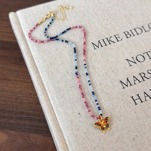 Détail d'un collier de perles colorées avec pendentif papillon émaillé sur un livre