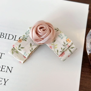 Detail view of handmade pink silk rose hair clip with floral ribbon on display card