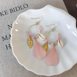 Detail view of bohemian feather drop earrings with pink beads and golden leaf charms