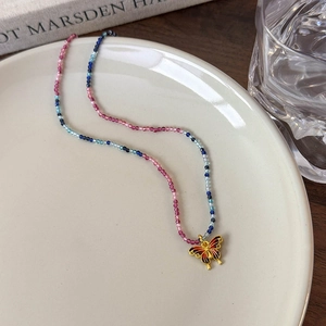 Détail d'un collier de perles colorées avec un pendentif papillon doré en émail