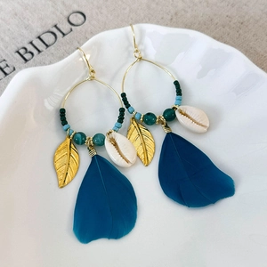 Detail of Bohemian feather earrings with golden leaf charms and natural seashells