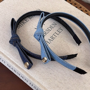 Blue denim bow headband with gold button detail shown on a vintage book background