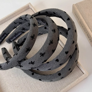 Three-piece grey headband set with black bow patterns and handmade tag on linen tray
