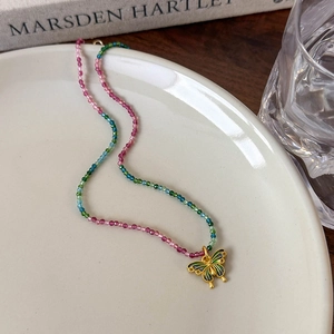 Détail d'un collier de perles colorées avec pendentif papillon émaillé vert sur plateau