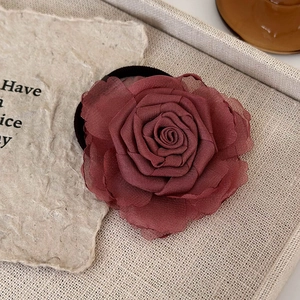 Detail of a handmade deep rose red fabric flower hair clip on a beige linen background