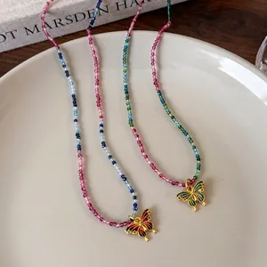Collier en perles colorées avec pendentif papillon émaillé sur un plat en céramique