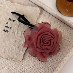 Detailed close-up of a handmade dark red fabric rose flower hair clip on a beige tray