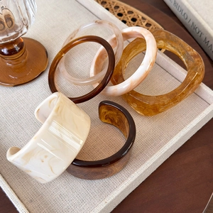 Irregular wide acrylic resin bracelets in amber and tortoiseshell patterns on linen tray