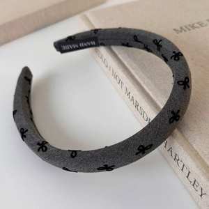 Detailed view of handmade gray fabric headband featuring embroidered black bow patterns