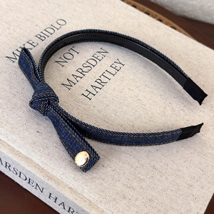 Detail of blue denim headband featuring bow with gold button and anti-slip teeth design