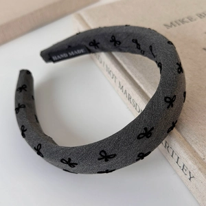 Detailed view of handmade grey headband with black embroidered bows and label