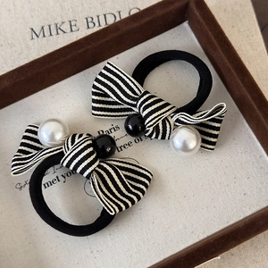 Elegant black and white striped bow hair tie with pearl accent on fabric tray
