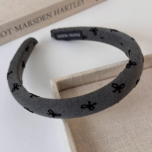 Close-up of handmade dark grey velvet headband with black bow patterns on woven tray