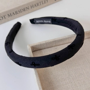Detail view of a handmade black velvet headband featuring a delicate bow and woven label