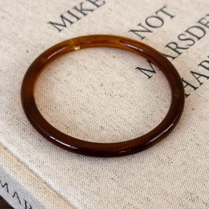 Close-up of translucent amber acrylic bangle with polished finish on a beige book