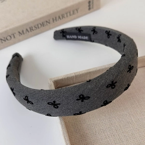 Detail view of a grey fabric headband featuring a black bow pattern and a Hand Made label