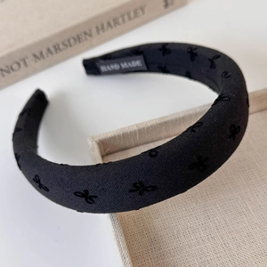 Detailed macro view of black flocked headband featuring hand-made woven label and bow embroidery