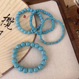 Vue détaillée de quatre bracelets en perles turquoise sur tissu beige avec un éventail classique