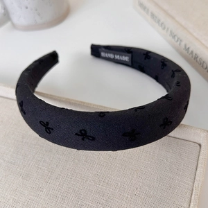 Close-up of thick black padded headband featuring embroidered bow and hand made label